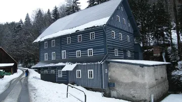 Das verschneite Holzgebäude der Janatův-Mühle in Buřany