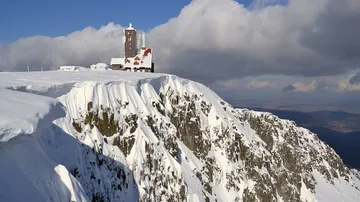 Verschneite Felswände der Schneegruben mit einem Gebäude auf dem Kamm